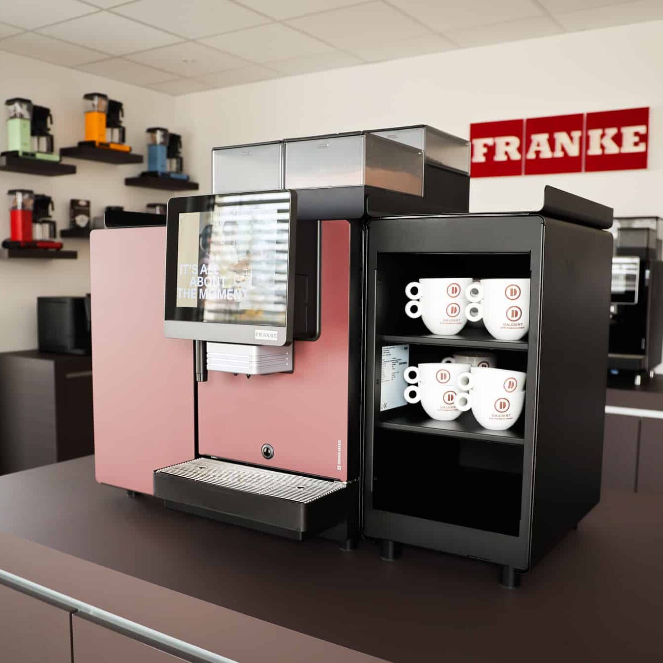 Franke Kaffeevollautomat mit Display und Daudert Kaffeetassen im Regal im Showroom