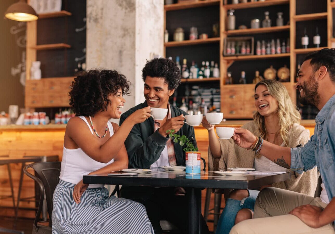 Young people sitting at cafe table and having coffee together. Group of friends making a toast with coffee.