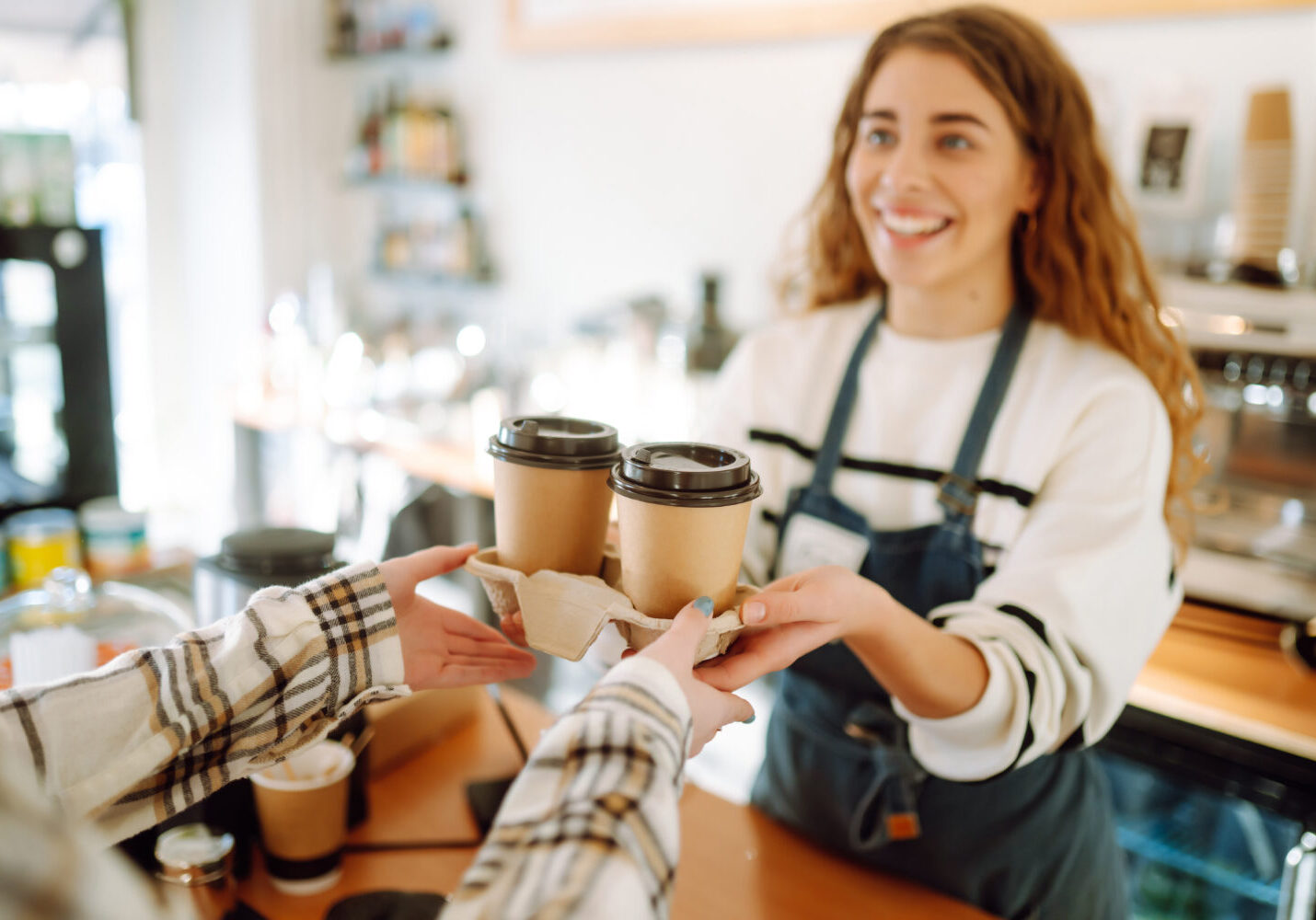 Smiling barista- girl giving take away coffee cups to a customers.